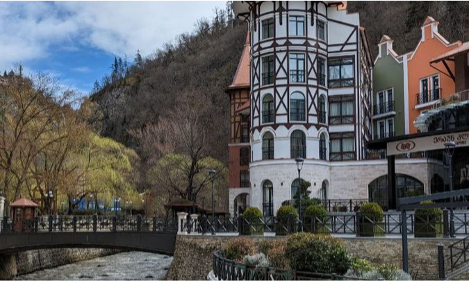 The illuminated fairy-tale architecture of a luxury hotel reflecting on the stone riverbanks of Borjomi town in Georgia at twilight during a bespoke private holiday with Lux Orient.