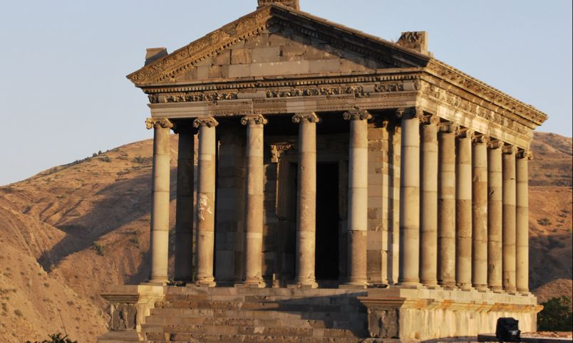 The ancient basalt stone pillars, triangular pediment, and classic columns of the Hellenistic Garni Temple in Armenia with arid mountains in the background during a luxury private heritage tour with Lux Orient.