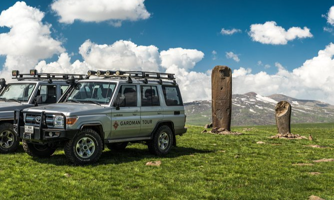 Premium silver off-road 4x4 expedition vehicles parked on a lush green mountain plateau next to ancient stone monoliths during a luxury private Jeep safari in Armenia with Lux Orient.