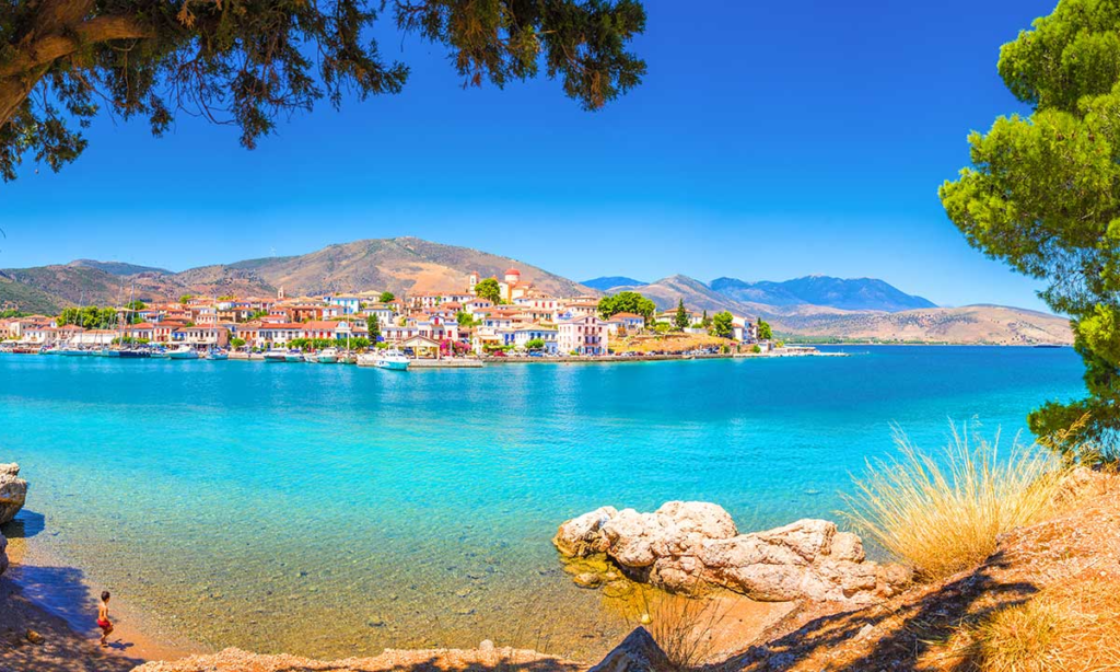 A sunny, elevated view of the colorful neoclassical captains' mansions lining the crystal-clear turquoise bay of Galaxidi town near Delphi during a luxury private tour with Lux Orient.