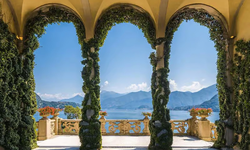The famous stone loggia and manicured ivy-covered arches of Villa del Balbianello overlooking the calm waters of Lake Como during a bespoke luxury private tour with Lux Orient.