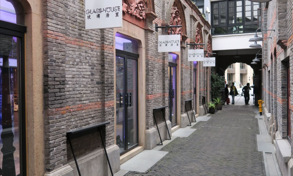 A narrow, historic brick lane framed by traditional grey Shikumen architecture and modern boutique signs in Shanghai's upscale Xintiandi district during a bespoke luxury city tour with Lux Orient.