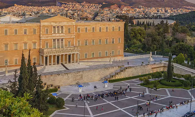 An elevated view of the historic neoclassical Greek Parliament building at Syntagma Square in Athens with a crowd gathered for a private bespoke city tour with Lux Orient.