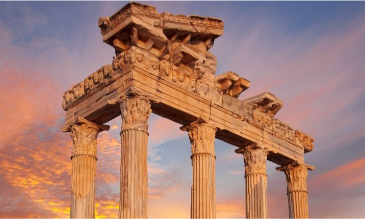 The five remaining fluted Corinthian columns and ornate architrave of the ancient Roman Temple of Apollo in Side against a dramatic pink and golden sunset sky during a luxury bespoke tour with Lux Orient.