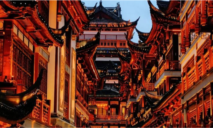 Intricately designed traditional Chinese wooden pavilions with sweeping multi-tiered roofs glowing with golden lights at dusk near the City God Temple in Shanghai during a luxury private cultural tour with Lux Orient.