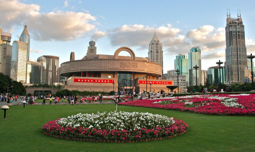 The unique circular building with a square base of the Shanghai Museum at People's Square, surrounded by manicured green lawns and vibrant flower beds during a luxury private cultural tour with Lux Orient.