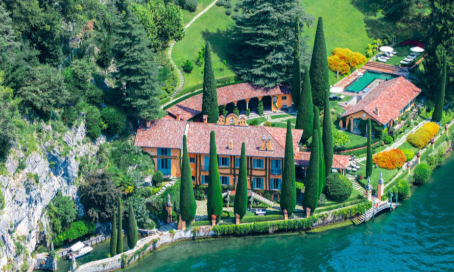 The magnificent ochre facade of the private estate Villa La Cassinella nestled amidst cypress trees and manicured gardens on the western shores of Lake Como during a luxury private boat cruise with Lux Orient.