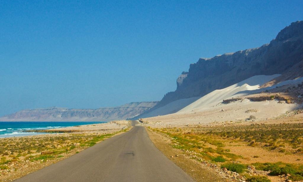 The towering, massive white sand dunes of Arher Beach leaning against sheer dark mountain cliffs on the shore of the ocean on Socotra Island, Yemen, during an exclusive private luxury tour with Lux Orient.