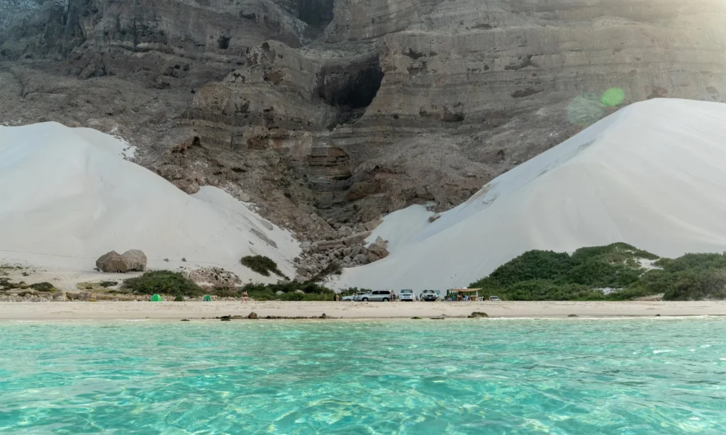 The towering, massive white sand dunes of Arher Beach leaning against sheer dark mountain cliffs on the shore of the ocean on Socotra Island, Yemen, during an exclusive private luxury tour with Lux Orient.