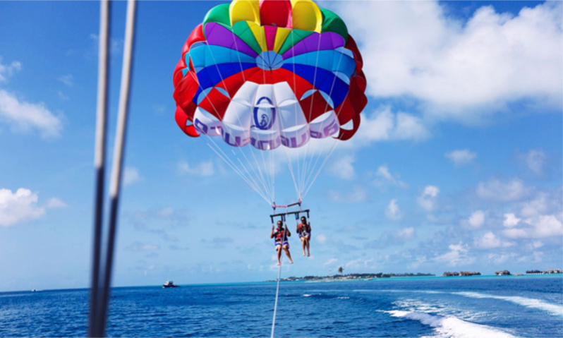 A vibrant parasail canopy soaring high in the blue sky above the modern coastal skyline, beaches, and azure waters of Batumi, Georgia during an exclusive private luxury excursion with Lux Orient.