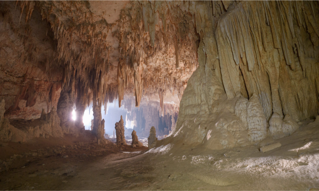 The massive, towering entrance of Hoq Cave looking out over the blue Arabian Sea on Socotra Island, Yemen, with the silhouette of a hiker standing among giant stalactites during a private luxury tour with Lux Orient.