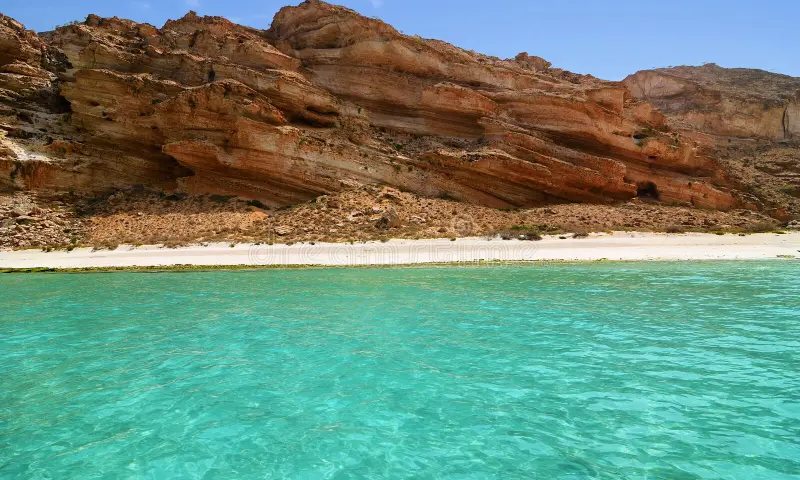 The massive, rugged limestone rock cliffs of Shuab Beach soaring out of the clear turquoise sea on Socotra Island, Yemen, during an exclusive private luxury boat cruise with Lux Orient.