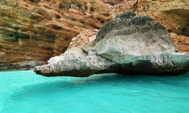 The massive, rugged limestone rock cliffs of Shuab Beach soaring out of the clear turquoise sea on Socotra Island, Yemen, during an exclusive private luxury boat cruise with Lux Orient.