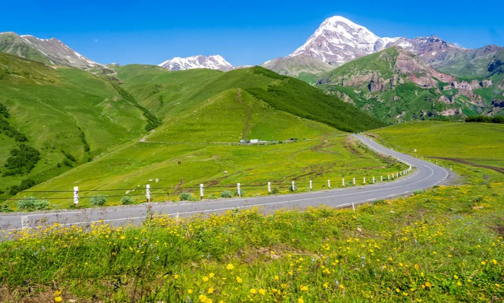 The dramatic winding asphalt road of the Georgian Military Highway carving through the massive green peaks and steep valleys of the Greater Caucasus Mountains in Georgia during an exclusive private luxury tour with Lux Orient.