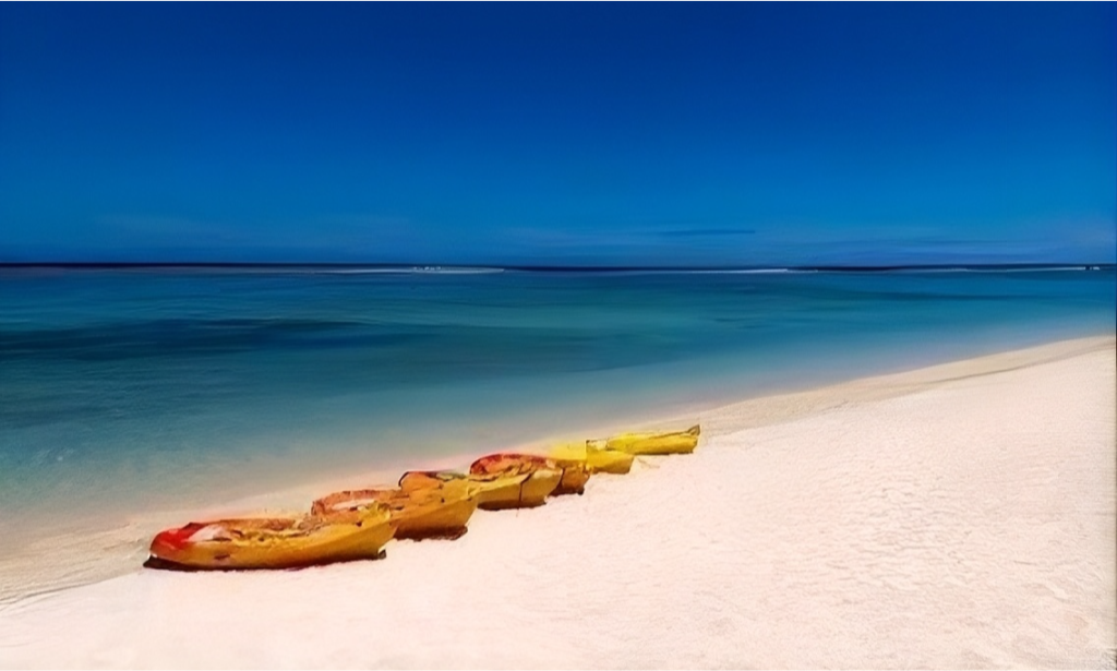 The pristine white sand shoreline and calm turquoise lagoon waters of L'Ermitage Beach lined with casuarina trees in Saint-Gilles-les-Bains, La Réunion, during an exclusive private luxury vacation with Lux Orient.