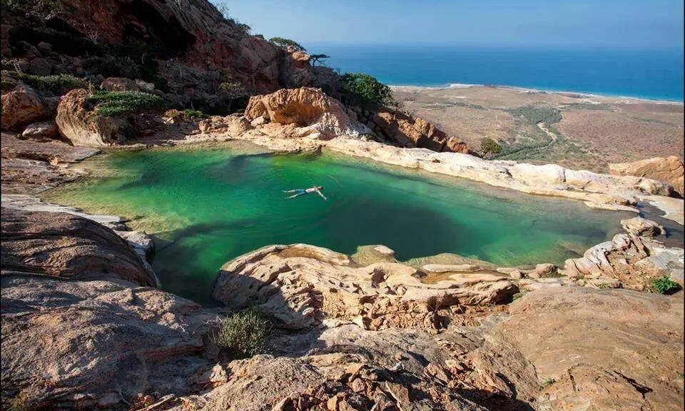 A natural stone freshwater infinity pool on a cliff edge overlooking the mountain valley and Arabian Sea in Homhil Protected Area on Socotra Island, Yemen, during an exclusive private luxury tour with Lux Orient.