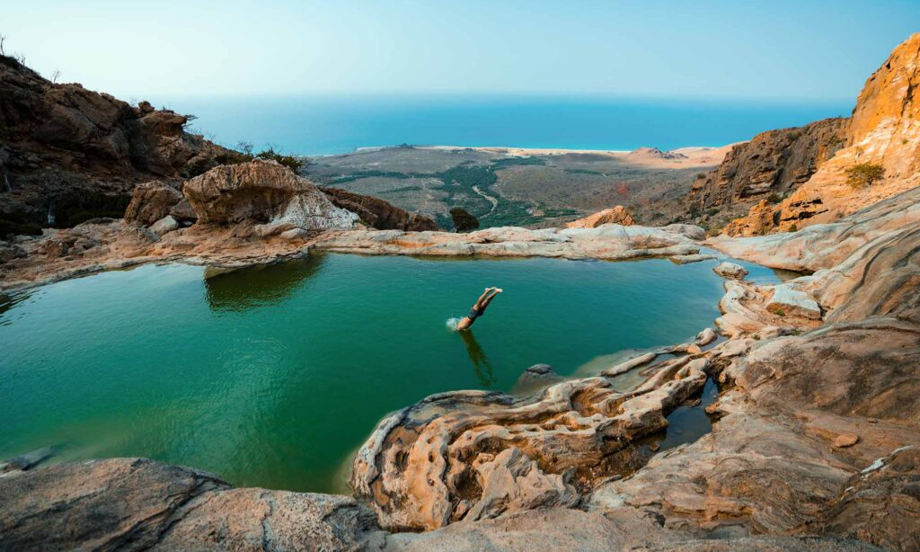 A natural stone freshwater infinity pool on a cliff edge overlooking the mountain valley and Arabian Sea in Homhil Protected Area on Socotra Island, Yemen, during an exclusive private luxury tour with Lux Orient.