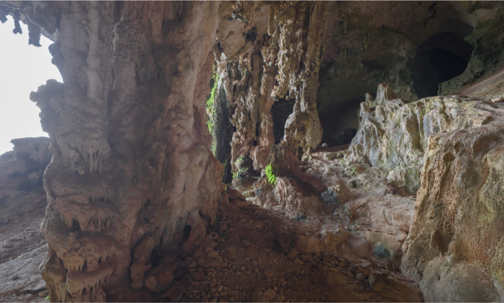 The massive, towering entrance of Hoq Cave looking out over the blue Arabian Sea on Socotra Island, Yemen, with the silhouette of a hiker standing among giant stalactites during a private luxury tour with Lux Orient.