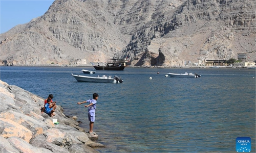 An aerial view of the isolated coastal houses of Kumzar village squeezed into a narrow valley floor beneath towering rocky mountains on the shore of Musandam, Oman, during a private luxury day tour with Lux Orient.