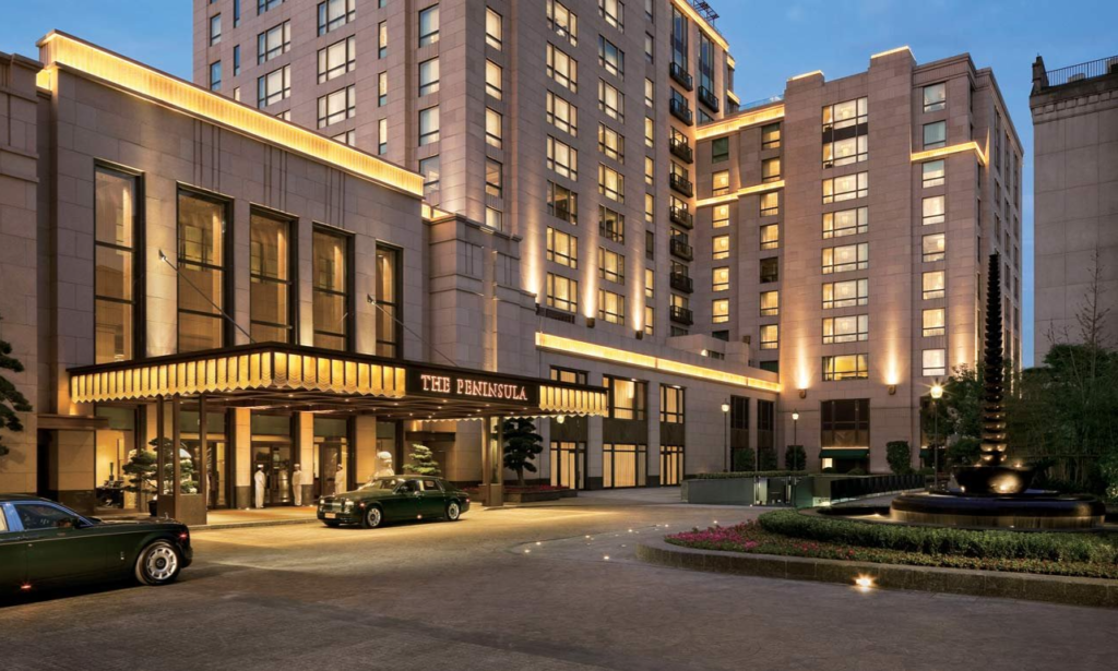 The majestic Art Deco granite facade of The Peninsula Shanghai hotel along the historic Bund overlooking the modern Pudong skyline, during an exclusive luxury vacation with Lux Orient.