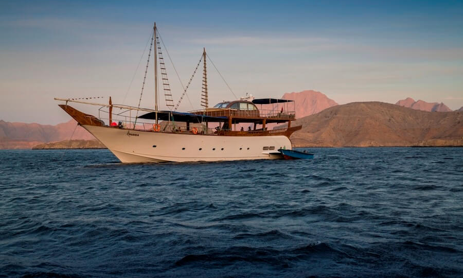 The premium multi-deck Omani Dhow Rubba sailing through the steep limestone cliffs of the fjords in Musandam, Oman, during an exclusive private luxury cruise with Lux Orient.