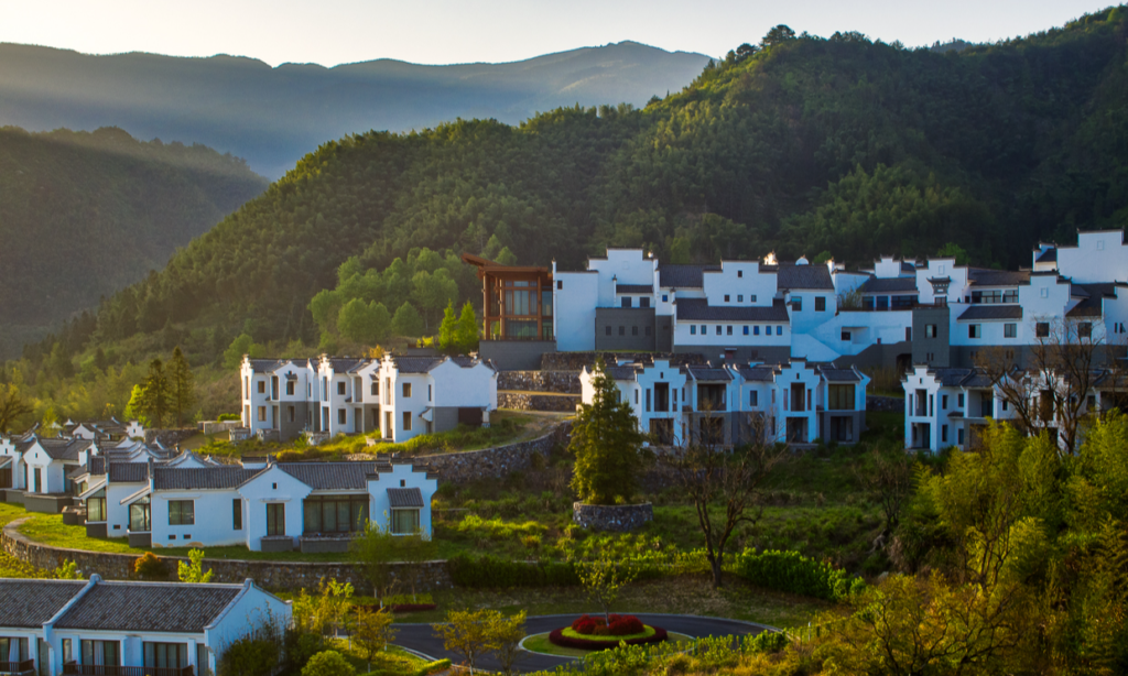 The elegant white walls and dark tiled roofs of traditional Hui-style villas at the luxury Banyan Tree Huangshan resort surrounded by lush green hills, during an exclusive private vacation with Lux Orient.
