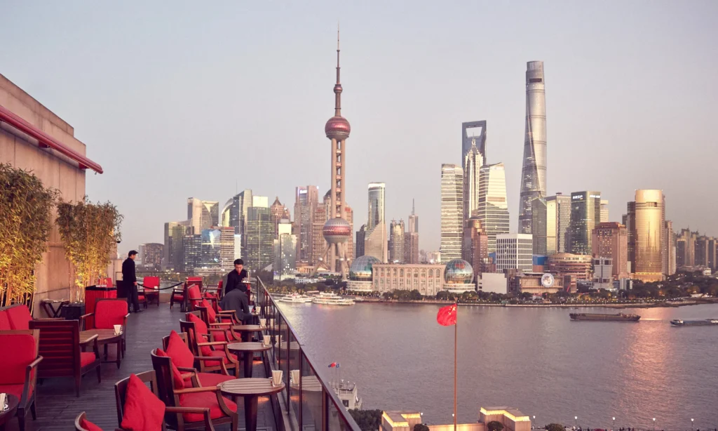 The majestic Art Deco granite facade of The Peninsula Shanghai hotel along the historic Bund overlooking the modern Pudong skyline, during an exclusive luxury vacation with Lux Orient.