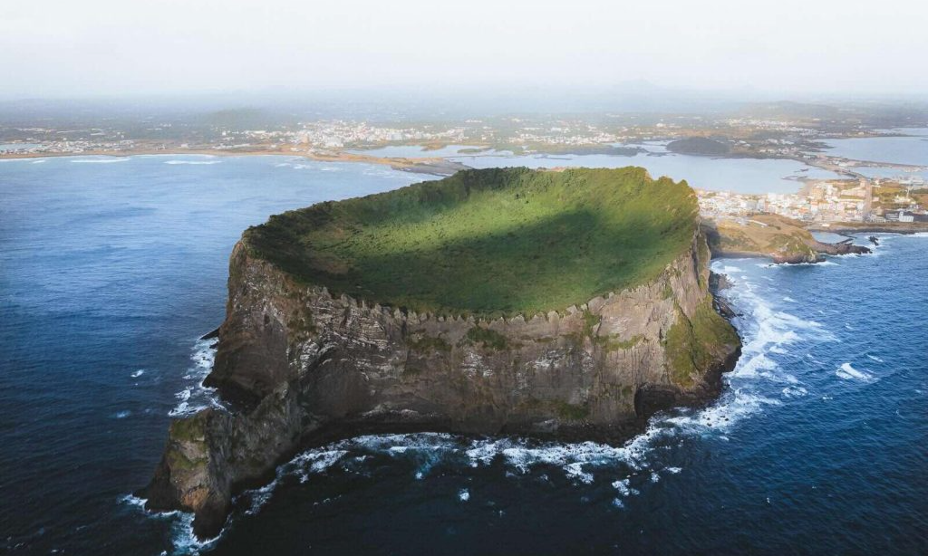 The green, bowl-shaped crater and jagged rock peaks of the massive Seongsan Ilchulbong volcanic tuff cone on Jeju Island, South Korea during a luxury private guided nature tour with Lux Orient.