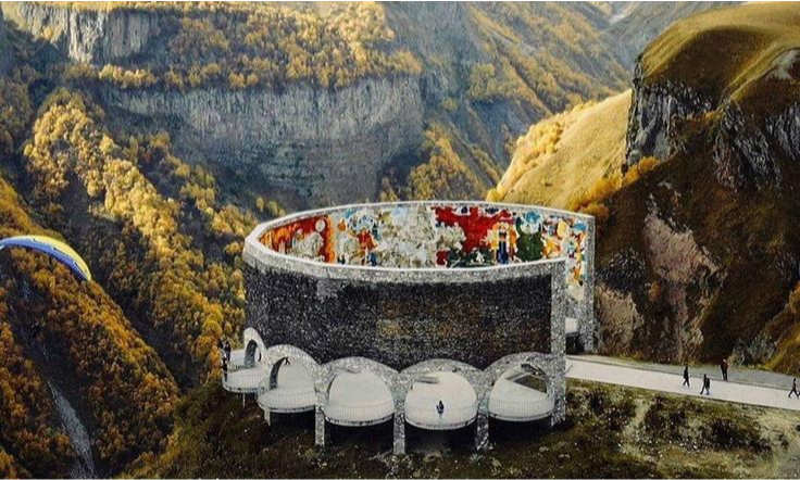 The massive, colorful mosaic concrete semi-circle architecture of the Gudauri Panorama monument overlooking the dramatic snow-capped mountains and steep valleys of Georgia during an exclusive private luxury tour with Lux Orient.