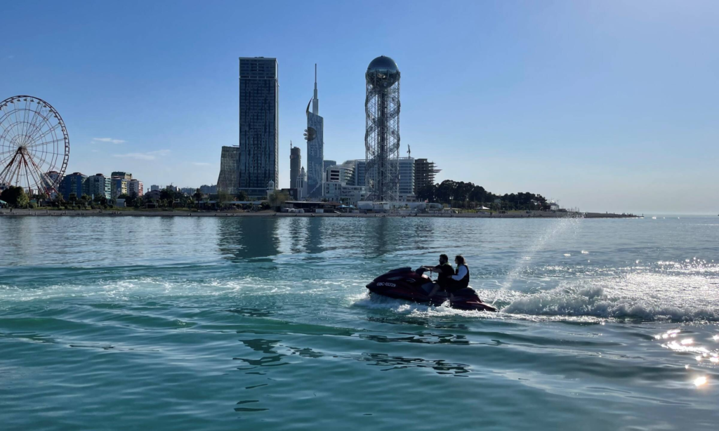A high-speed luxury jet ski carving a white water wake through the azure waves of the Black Sea with the futuristic city skyscrapers of Batumi, Georgia in the background during an exclusive private excursion with Lux Orient.