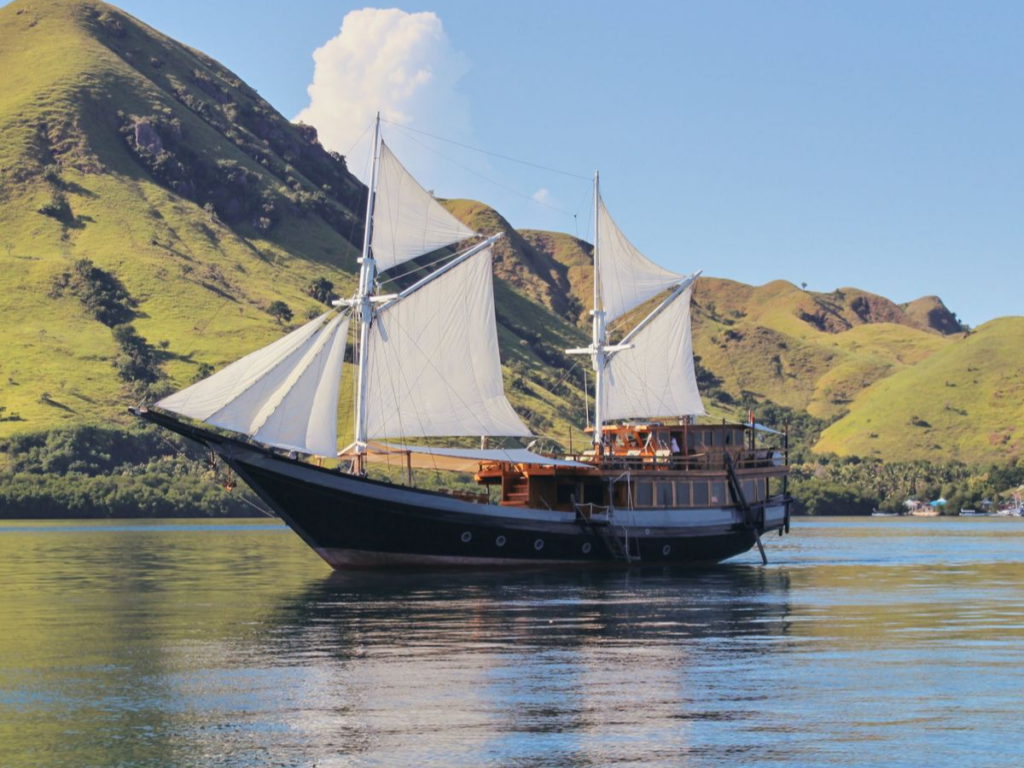 A magnificent traditional wooden phinisi yacht with its large sails unfurled, cruising through the turquoise waters and volcanic islands of Komodo National Park near Labuan Bajo, Indonesia, during an exclusive private charter with Lux Orient.
