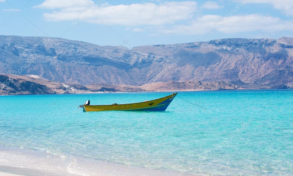 A traditional wooden dhow boat cruising through the crystal-clear turquoise waters of the Arabian Sea toward the white sands of Shuab Beach on Socotra Island, Yemen, during an exclusive private luxury tour with Lux Orient.