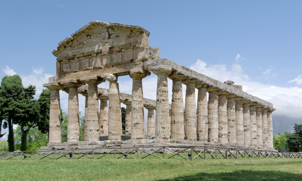 The massive stone columns and preserved triangular pediment of an ancient Greek Doric temple on a grassy field during a luxury private historical tour tracking classical roots back to Athens with Lux Orient.