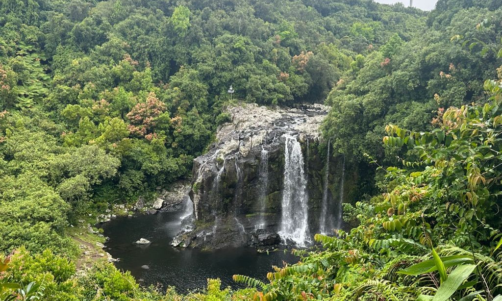 A tranquil freshwater waterfall plunging into the clear, green volcanic waters of Bassin Bœuf surrounded by lush tropical jungle in Sainte-Suzanne, La Réunion, during an exclusive private luxury tour with Lux Orient.