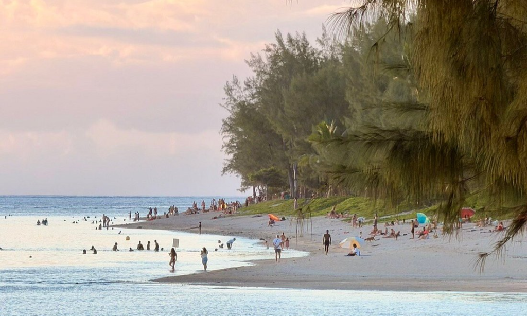 The pristine white sand shoreline and calm turquoise lagoon waters of L'Ermitage Beach lined with casuarina trees in Saint-Gilles-les-Bains, La Réunion, during an exclusive private luxury vacation with Lux Orient.
