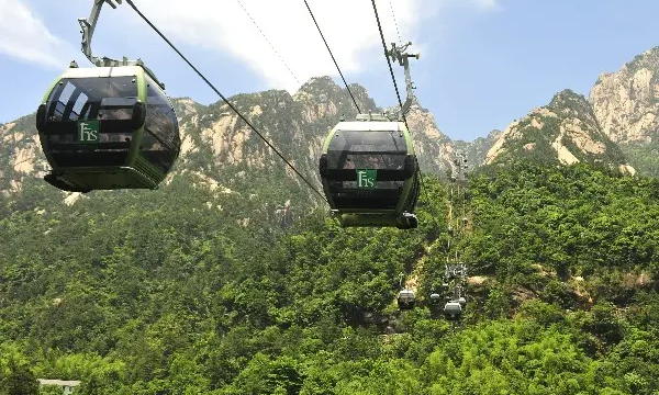 A modern glass cable car of the Yungu Cableway moving quietly past the dramatic, mist-covered mountain cliffs and pine trees of Huangshan, during an exclusive private luxury tour with Lux Orient.