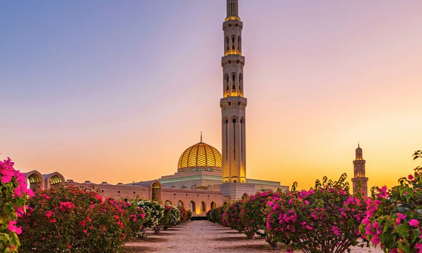 The majestic sandstone exterior and central golden dome of the Sultan Qaboos Grand Mosque flanked by soaring minarets in Muscat, Oman, captured during an exclusive private luxury heritage tour with Lux Orient.