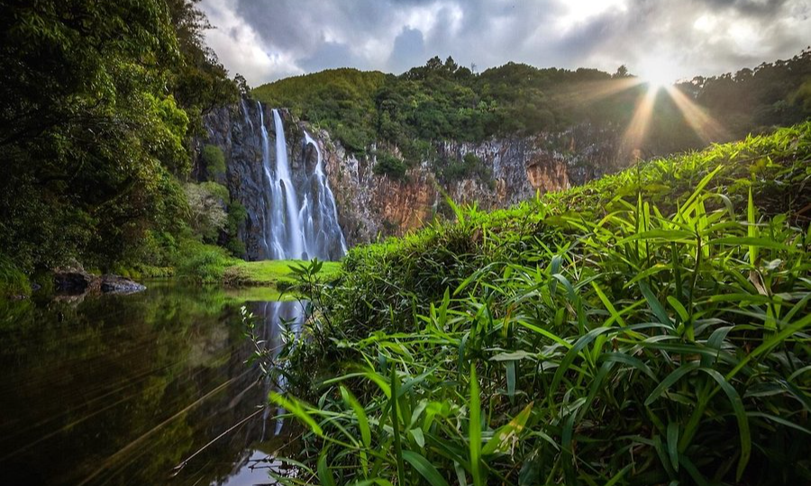 The dramatic, roaring white waters of Cascade Niagara waterfall cascading down a lush, green volcanic cliff into a natural pool in Sainte-Suzanne, La Réunion, during an exclusive private luxury tour with Lux Orient.