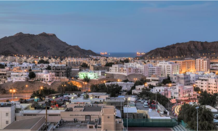 The striking white facade and defensive towers of the historic Sohar Fort surrounded by green palm trees in Sohar Town, Oman, during an exclusive private luxury heritage tour with Lux Orient.